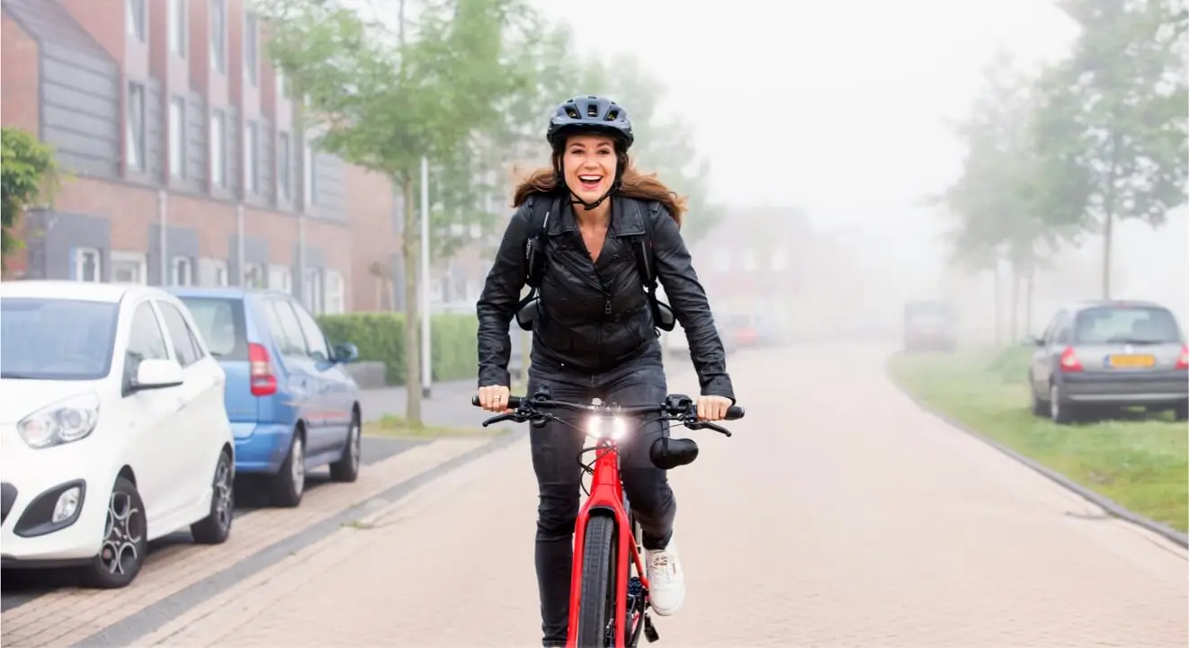 Een vrouw met helm rijdt op een rode e-bike door een woonstraat